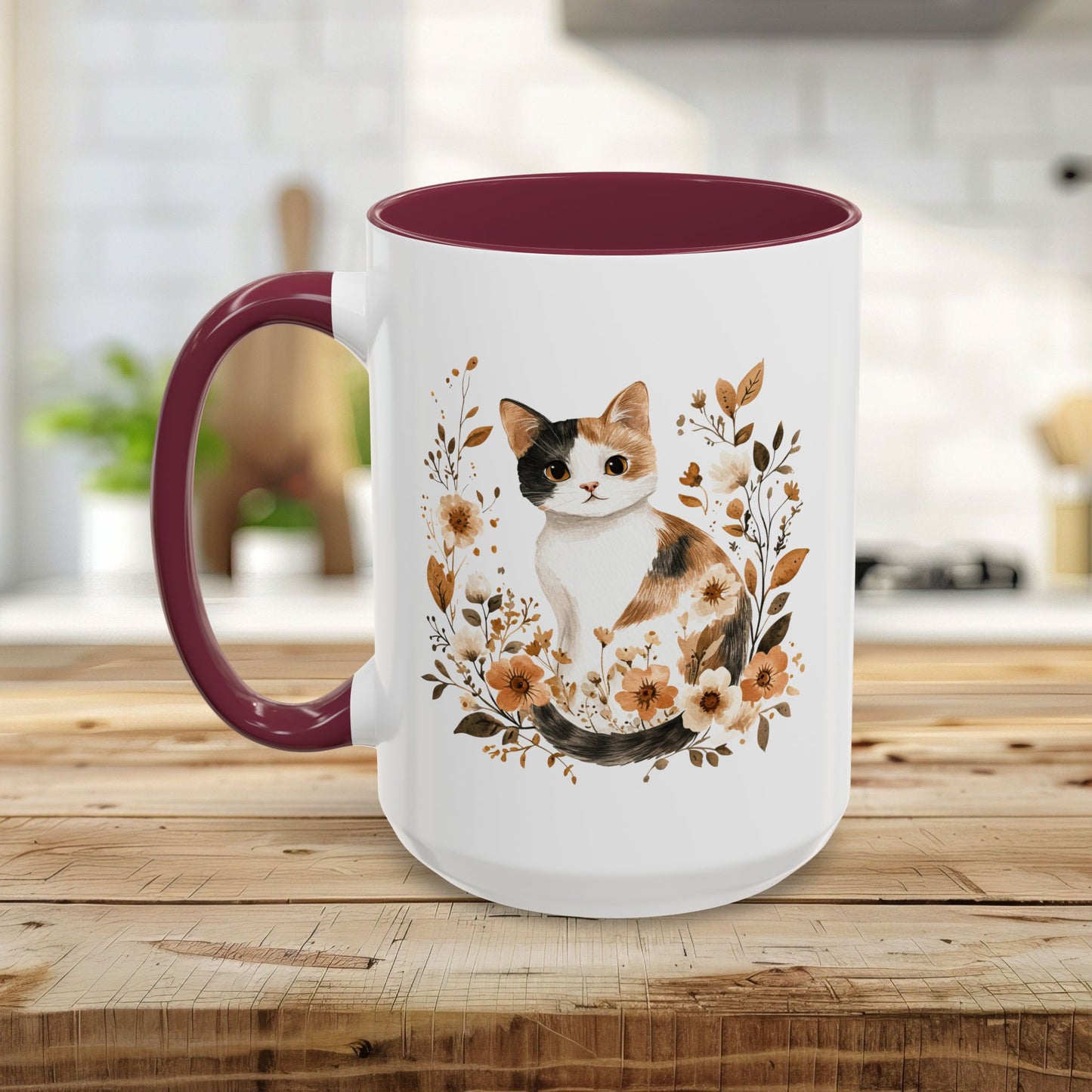 White ceramic mug with a watercolor calico cat surrounded by autumnal florals, featuring a contrasting maroon interior and handle.