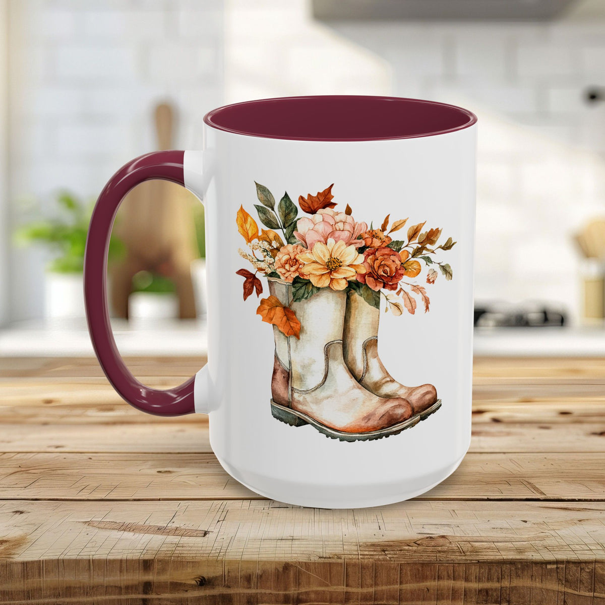 White ceramic mug with a burgundy handle and interior, featuring a watercolor design of worn boots overflowing with autumn flowers.