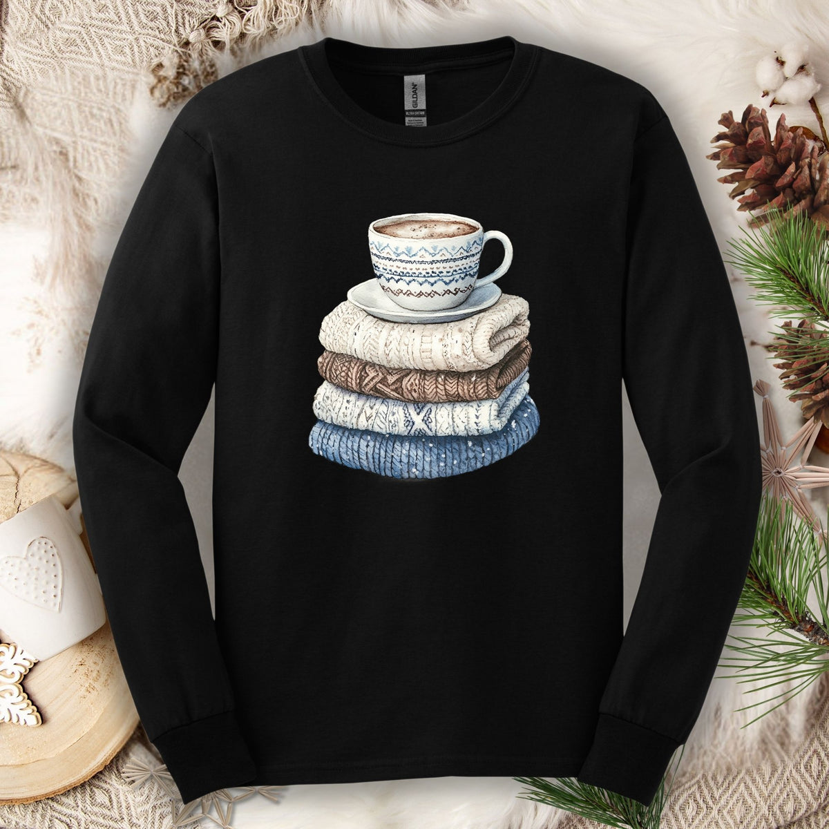 Black long-sleeve cotton tee with a cozy illustration of a steaming coffee mug atop stacked knit sweaters.
