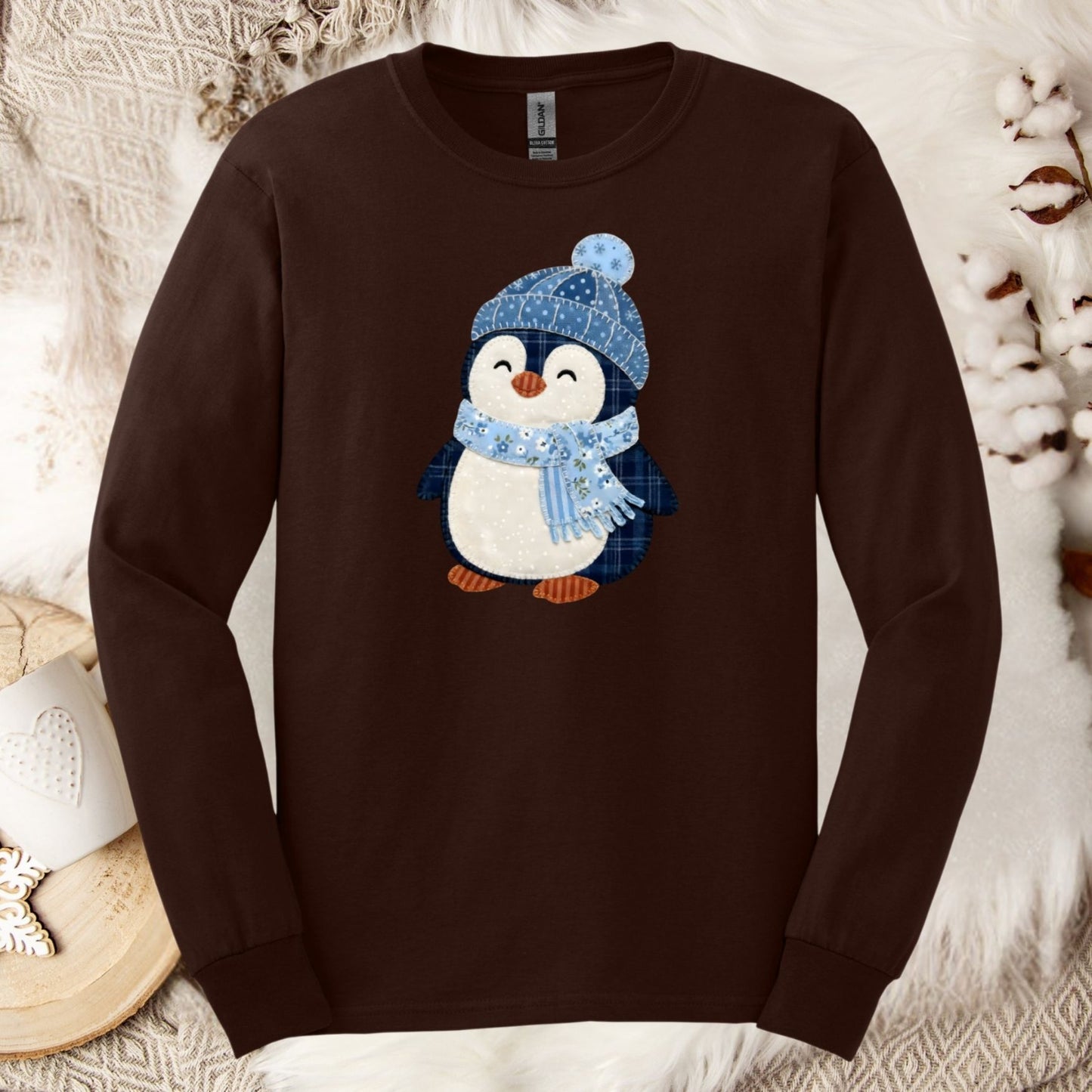 Brown long-sleeve tee with a faux patchwork winter penguin wearing a blue hat and scarf.
