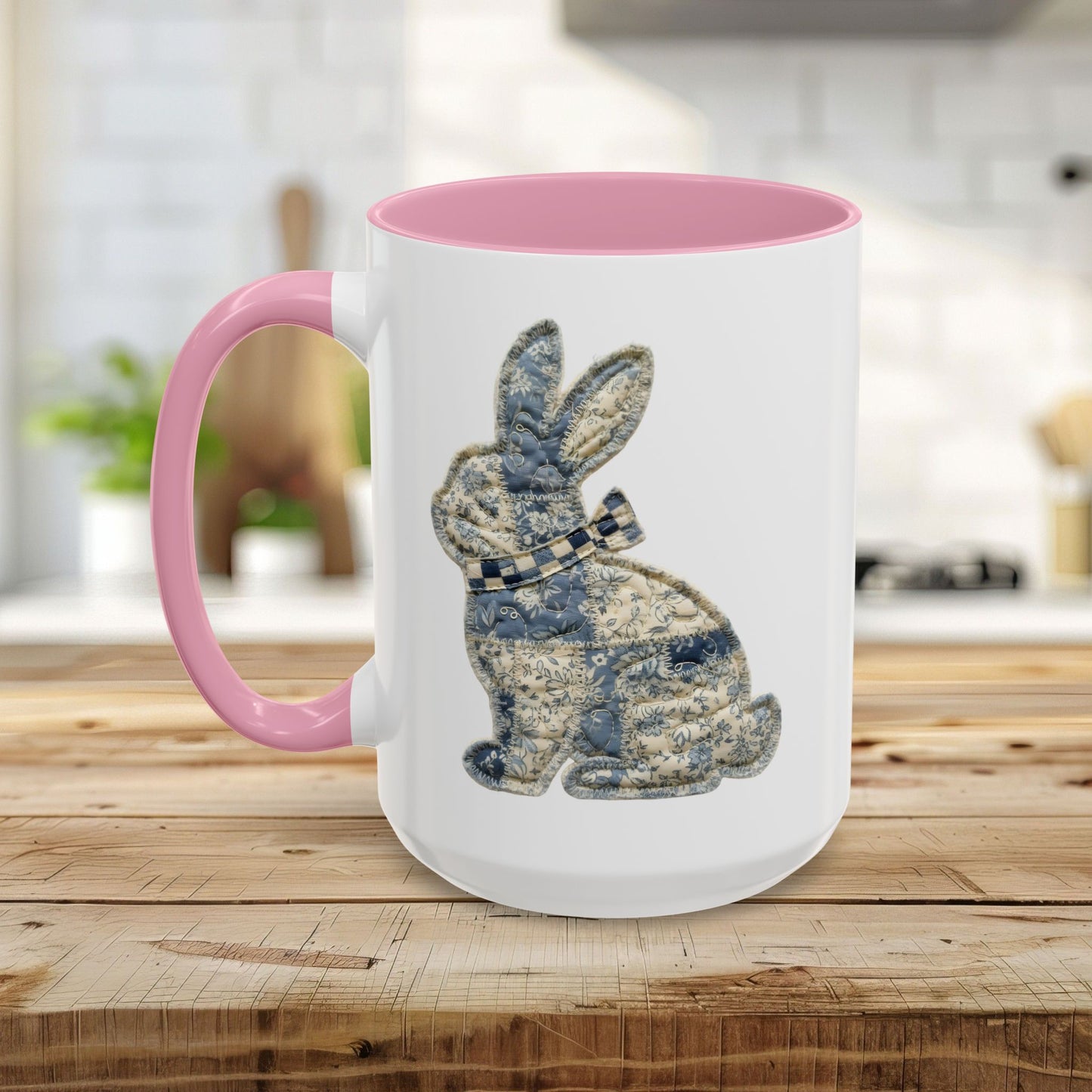 White ceramic coffee mug with pink handle and interior, featuring a blue and stone patchwork bunny illustration.