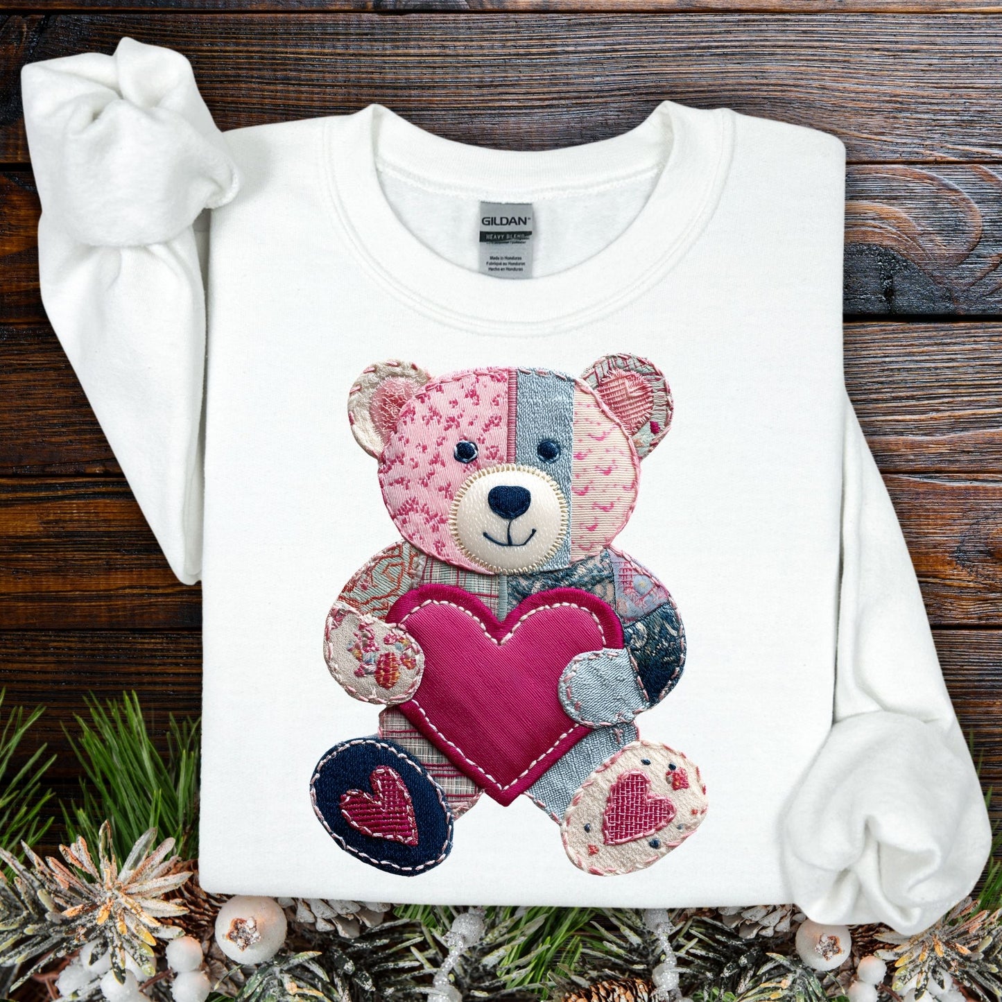 White Faux Patchwork Valentine's Teddy Bear Sweatshirt with a pink heart, on a rustic wood background.