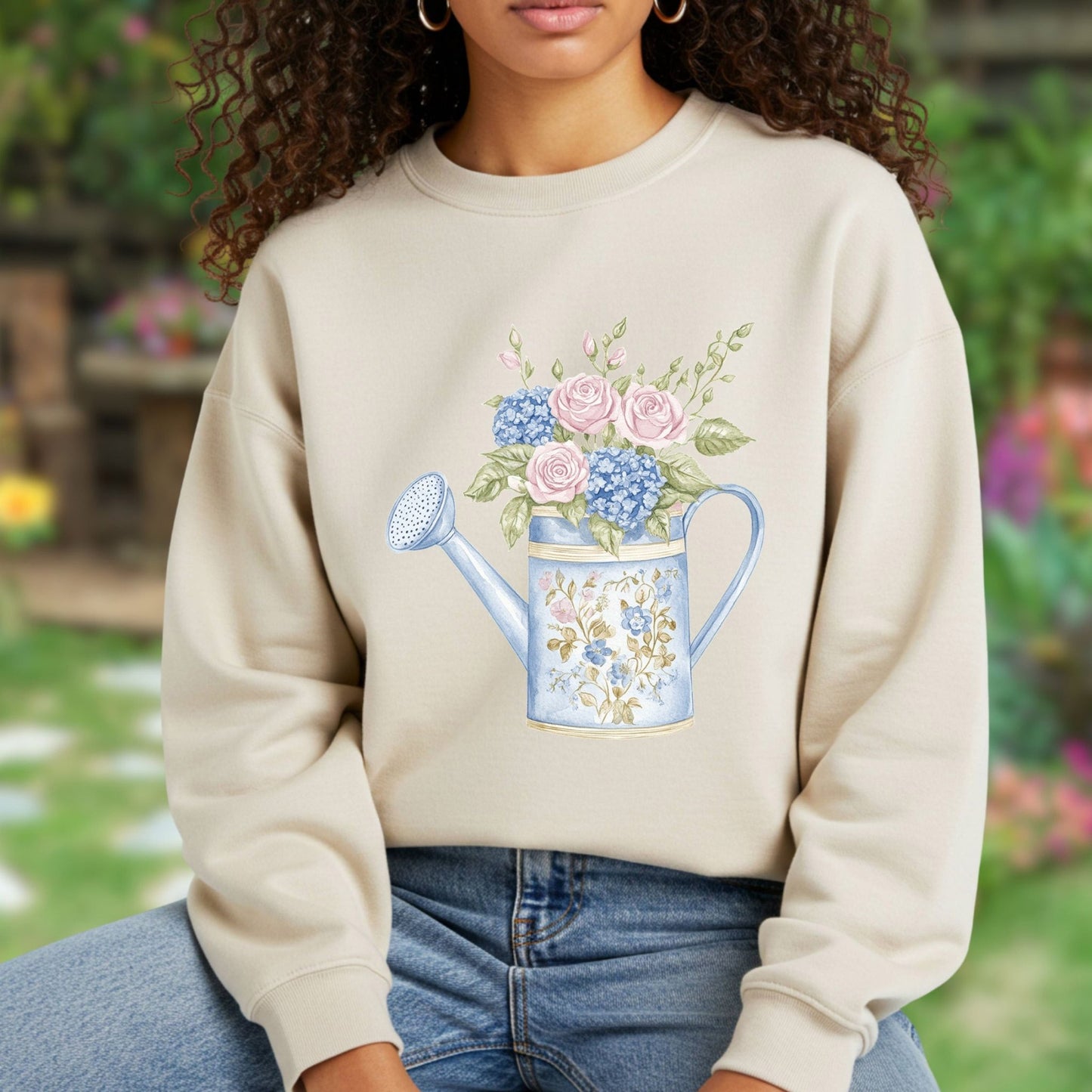 Beige crewneck sweatshirt with a watercolor floral watering can design, featuring pink roses and blue hydrangeas.