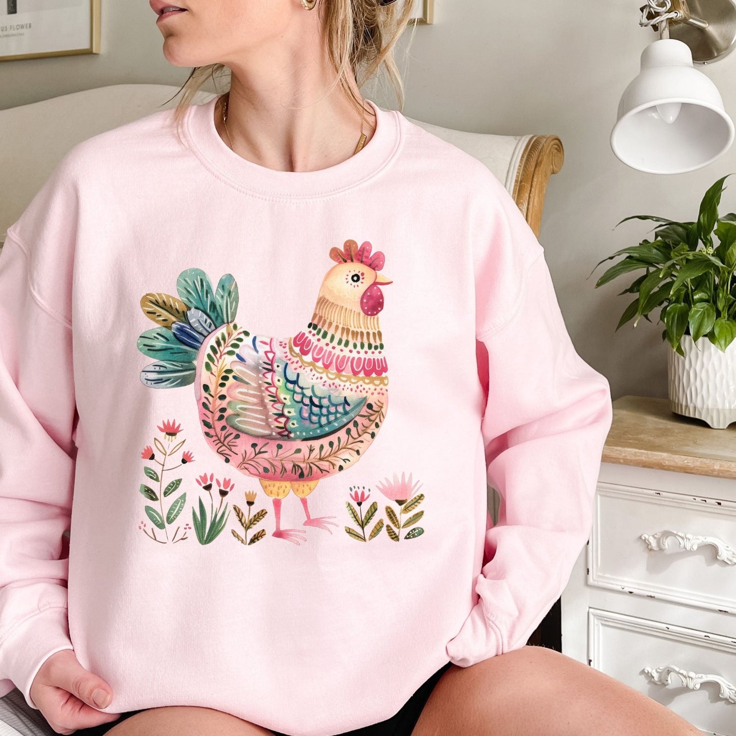 Pink crewneck sweatshirt with a colorful folk-art chicken and floral design.