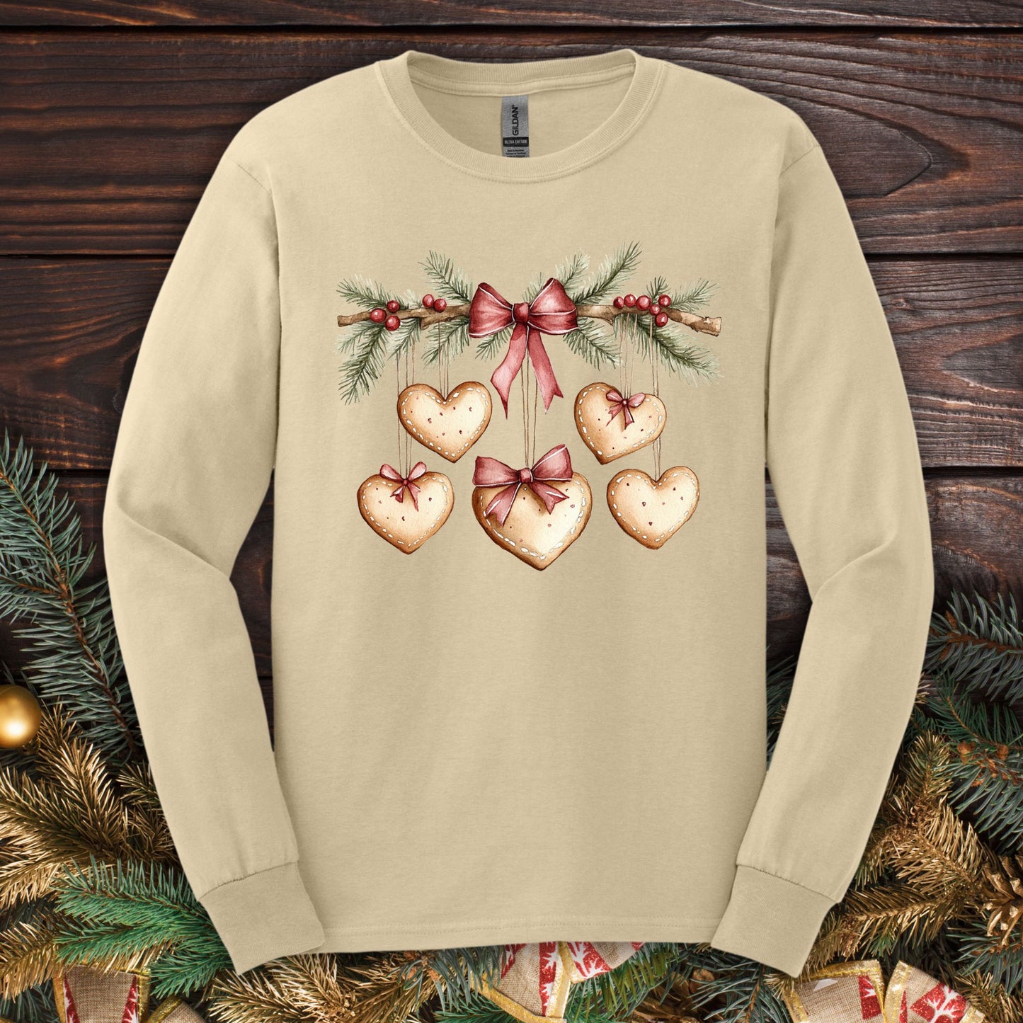 Sand long-sleeve tee with a watercolor gingerbread heart garland design, ribbed cuffs, and double-stitched hems.