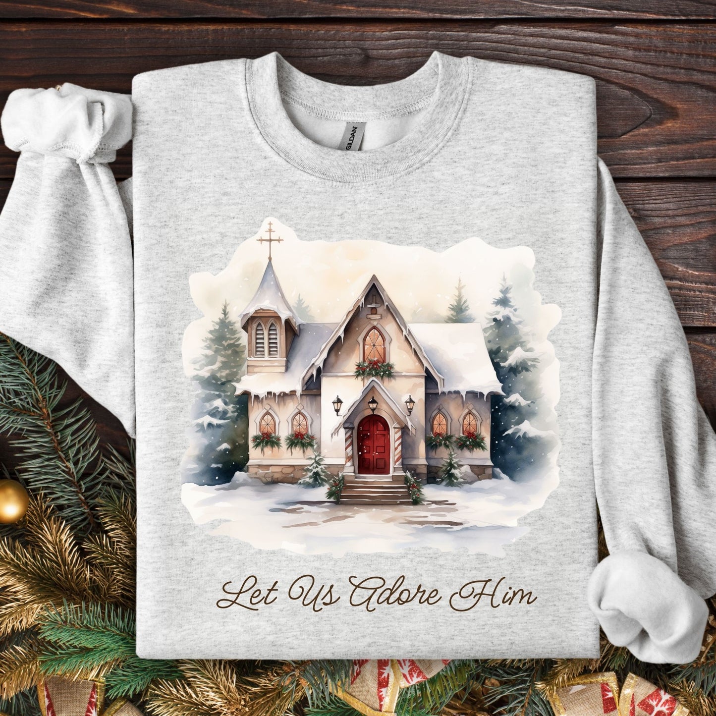 Ash Gildan sweatshirt with a snowy country chapel, garlands, wreaths, and "Let Us Adore Him" text.