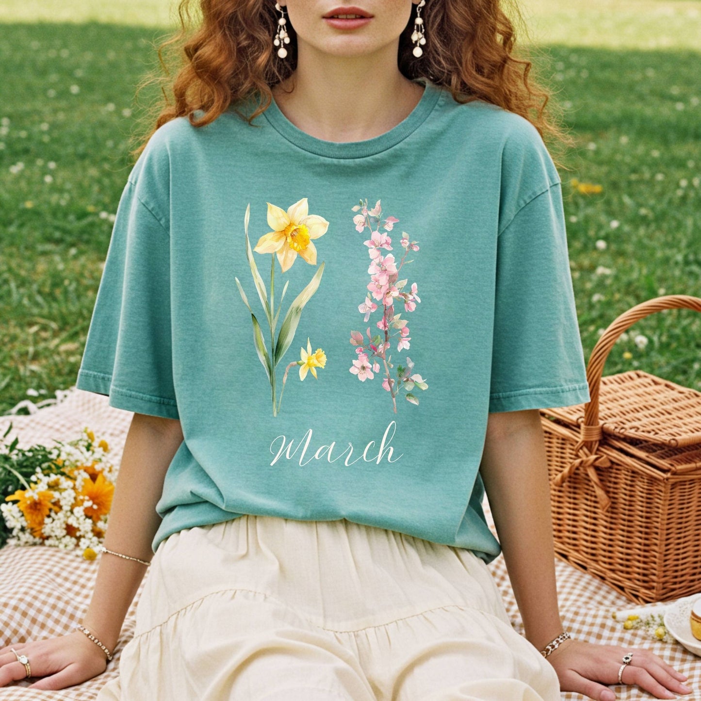 Garment-dyed teal t-shirt with watercolor daffodil, cherry blossoms, and "March" script.