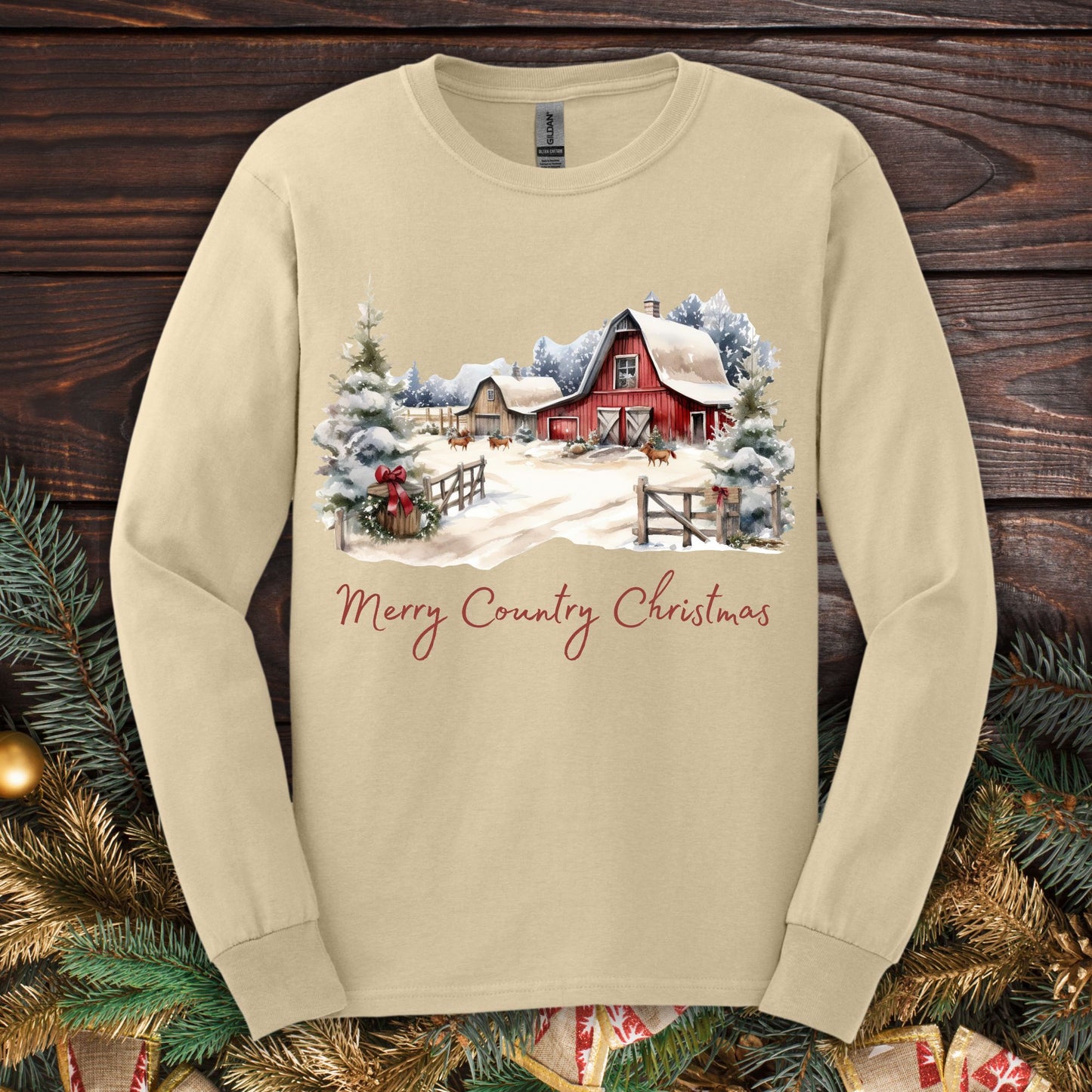 Sand long sleeve tee with a snowy red barn, festive greenery, and "Merry Country Christmas" text.
