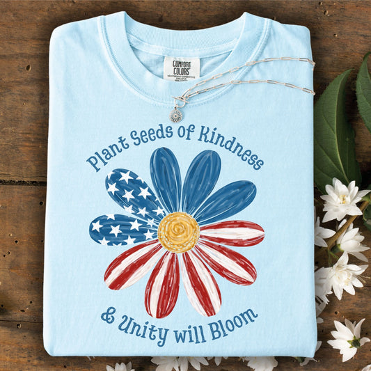 Chambray blue Comfort Colors t-shirt with "Plant Seeds of Kindness & Unity will Bloom" text and a daisy with an American flag design.