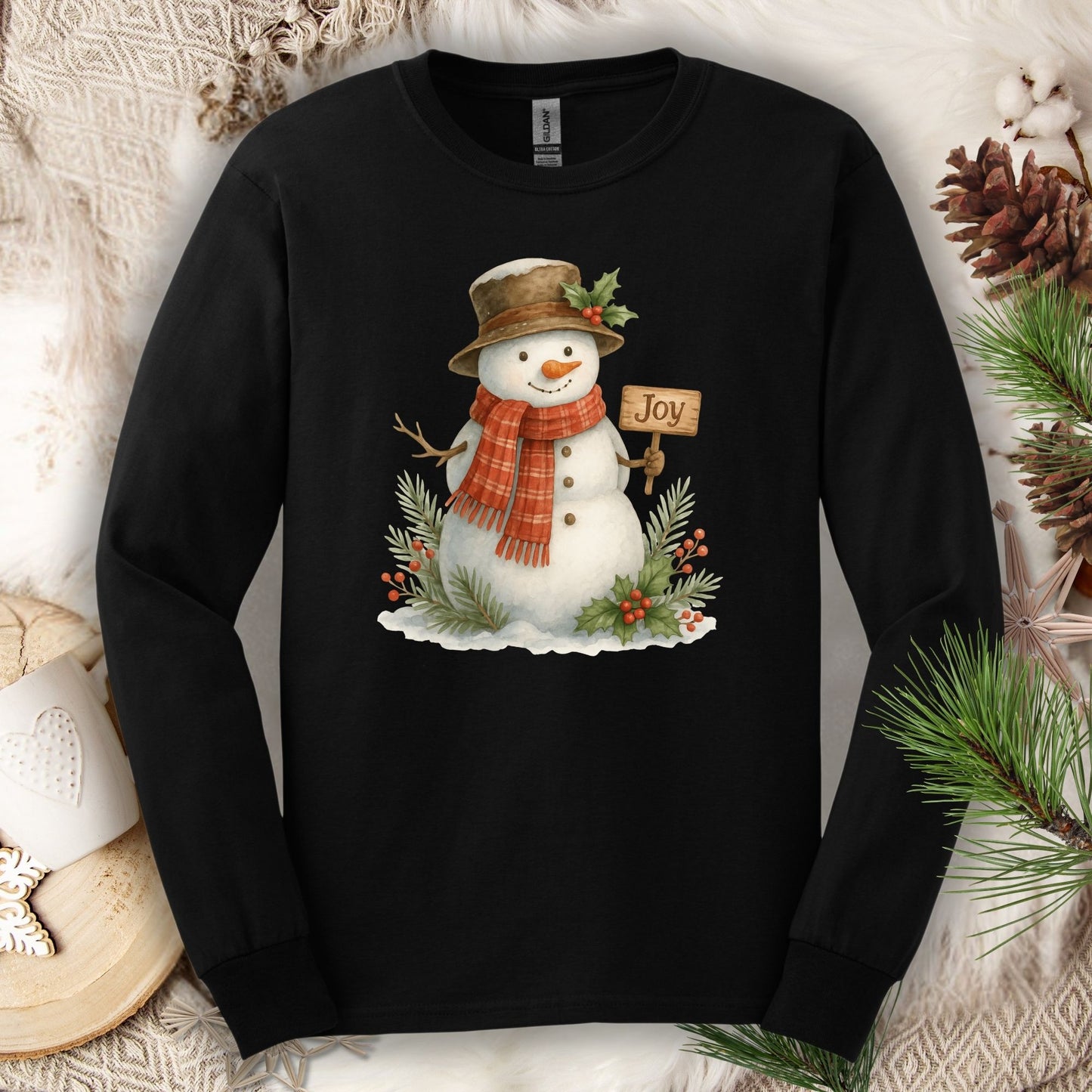 Black long sleeve tee with a watercolor snowman holding a "Joy" sign, holly, and snowy branches.