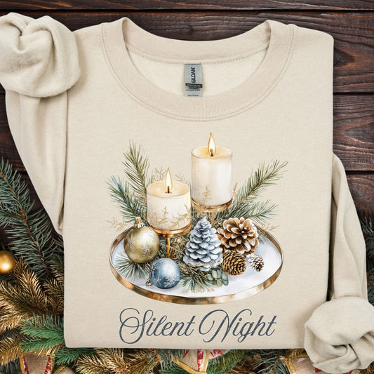 Sand Gildan sweatshirt with watercolor Silent Night advent arrangement: candles, pinecones, evergreens, blue/cream ornaments.