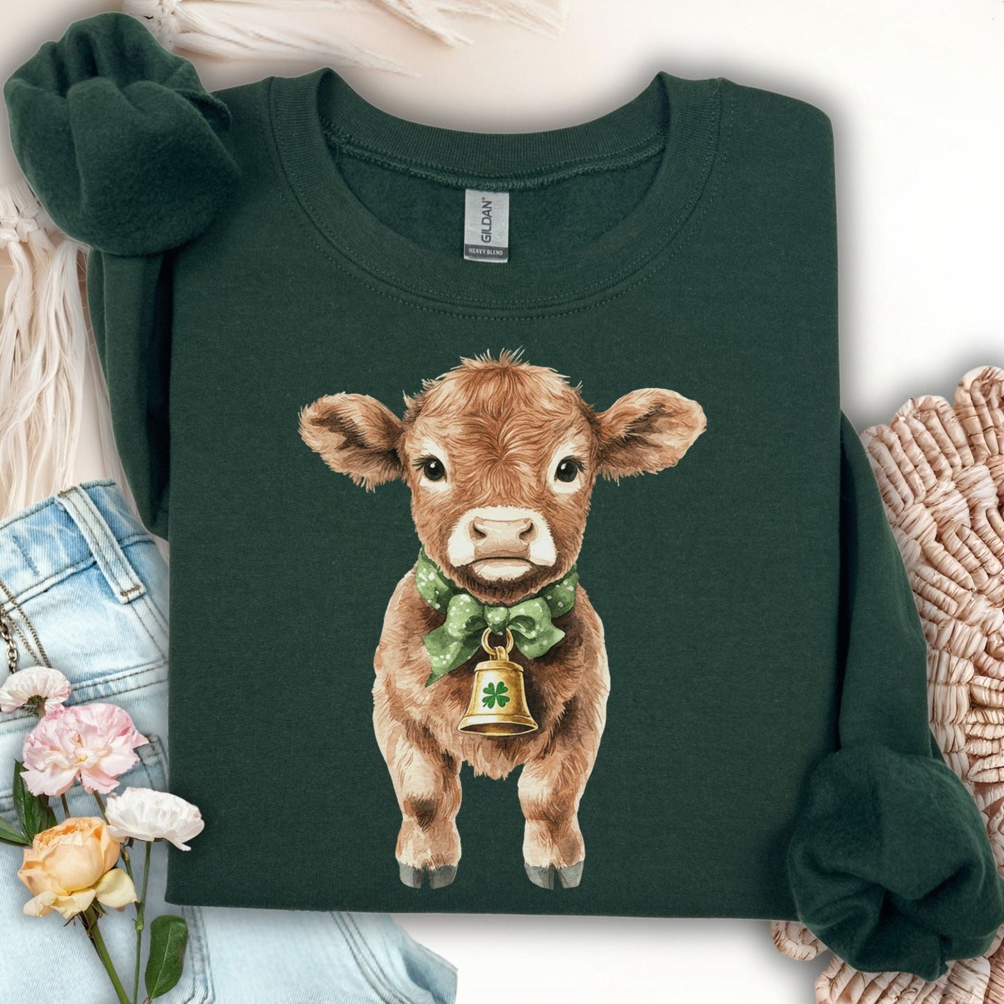 Dark green crewneck sweatshirt with a watercolor baby Highland cow wearing a green bow and clover bell.