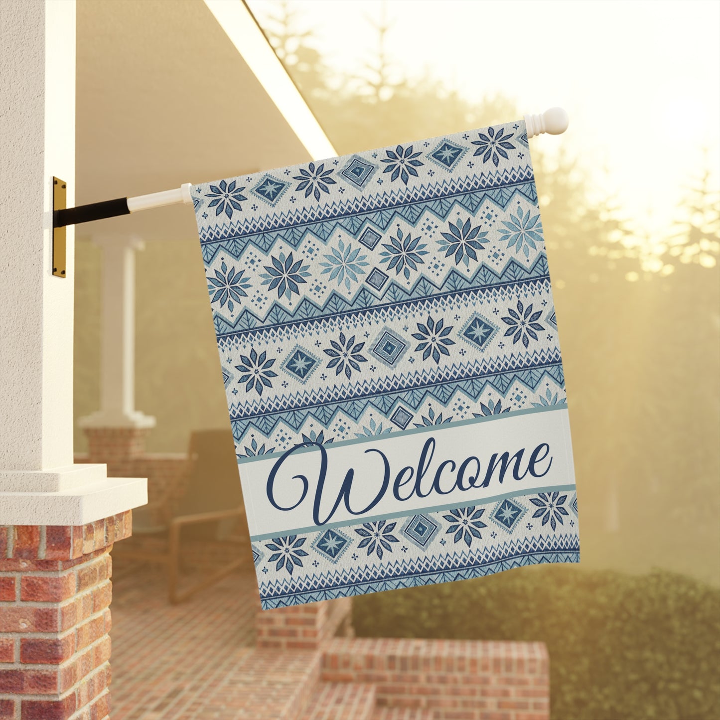 Blue Fair Isle poly poplin garden flag with "Welcome" script, hanging from a porch pole.