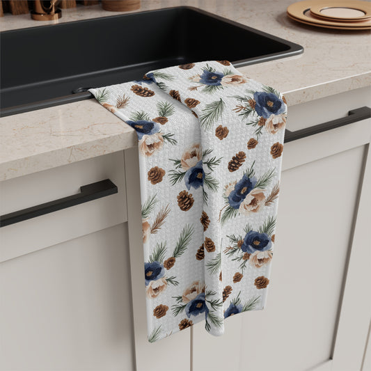 Microfiber tea towel with navy florals, pine sprigs, and pinecones draped over a kitchen counter.