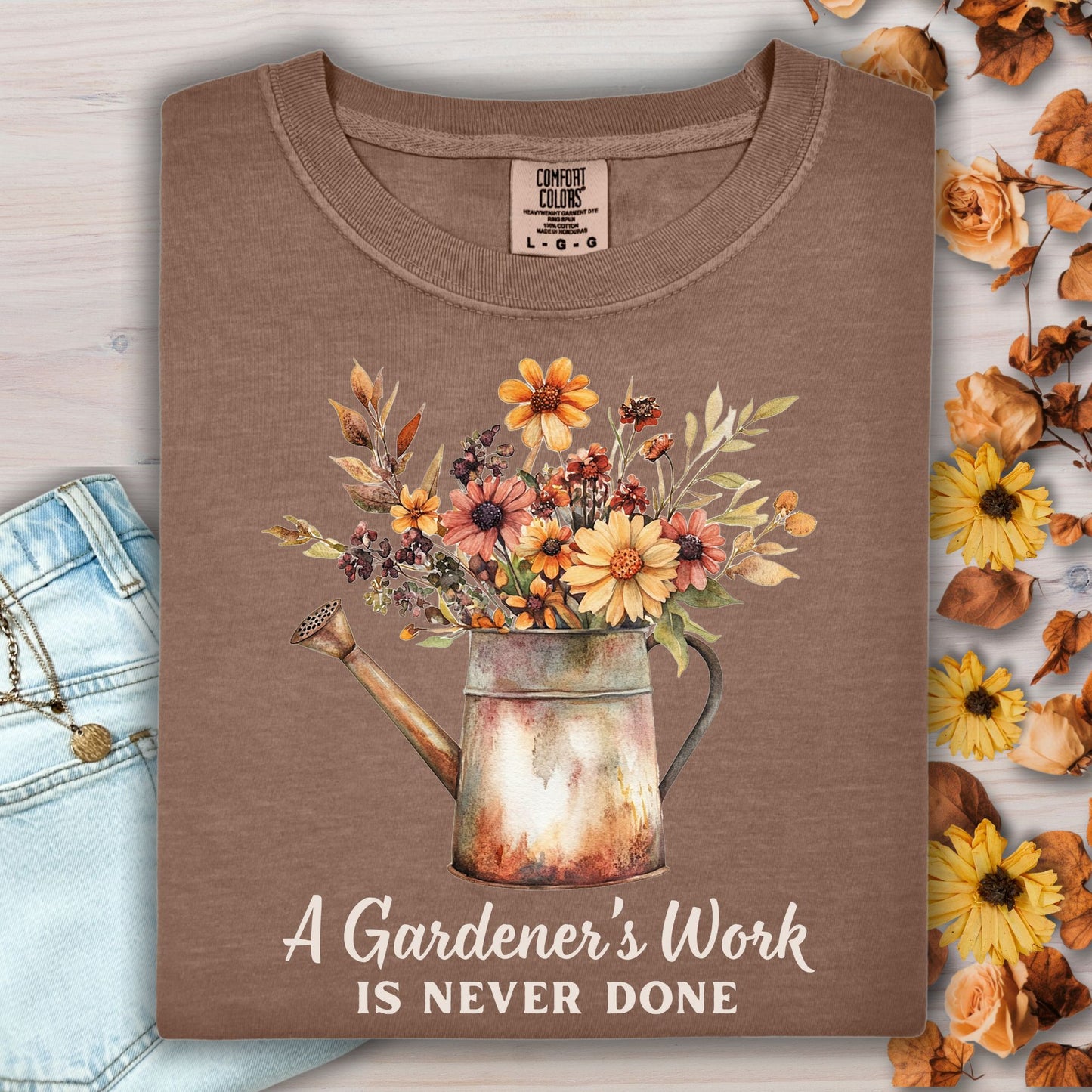 Espresso Comfort Colors tee with a watering can full of fall flowers and "A Gardener's Work Is Never Done" text.