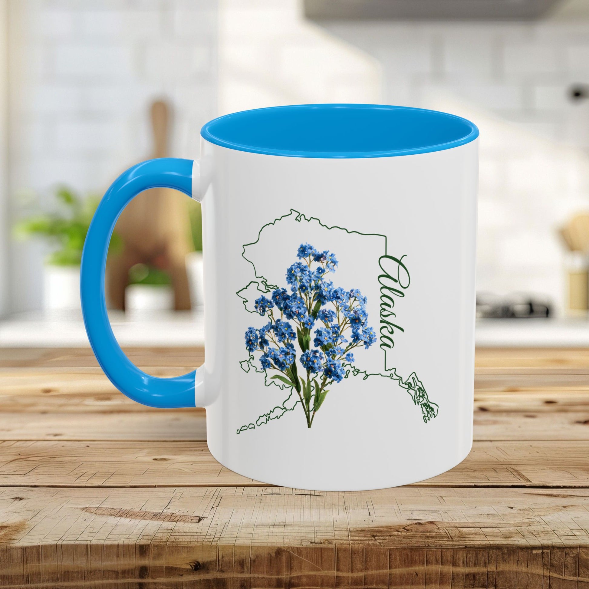 White ceramic mug with blue interior and handle, featuring an Alaska map outline and Alpine Forget-Me-Not flowers.