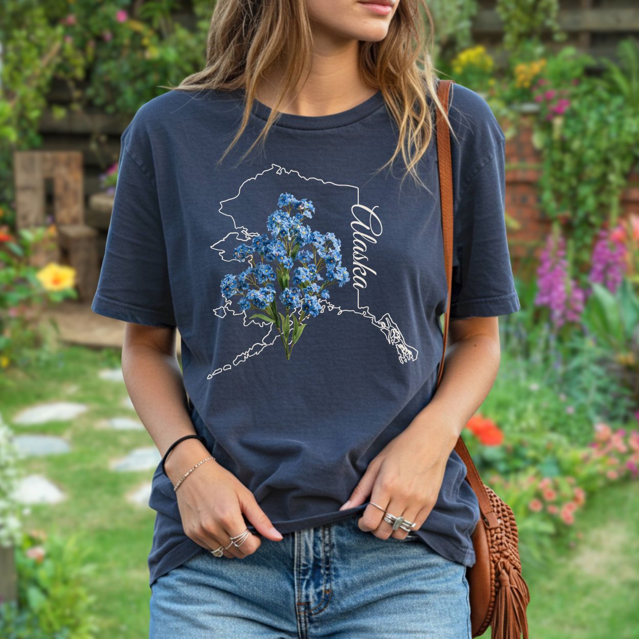 Garment-dyed navy t-shirt with a white outline of Alaska and blue forget-me-not flowers.