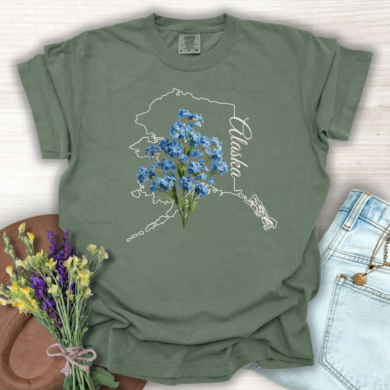 Moss green, relaxed-fit cotton t-shirt with an Alaska outline and blue forget-me-not flowers.