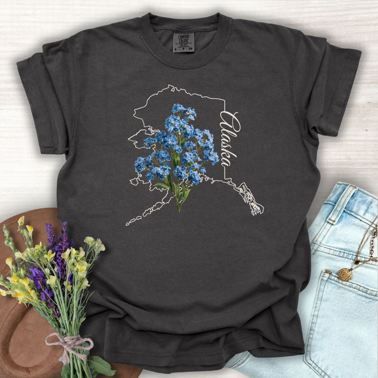 Pepper S-sized cotton t-shirt with white Alaska outline and blue forget-me-not flowers.