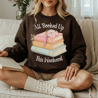 Woman in a brown "All Booked Up This Weekend" sweatshirt with watercolor books, reading on a sofa.