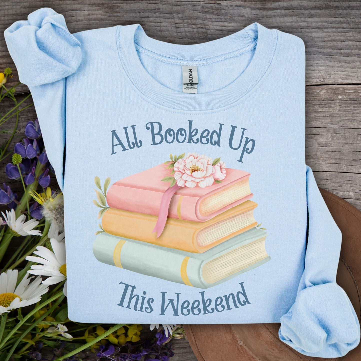 Light blue crewneck sweatshirt with "All Booked Up This Weekend" text and watercolor stack of books.
