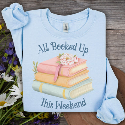 Light blue crewneck sweatshirt with "All Booked Up This Weekend" text and watercolor stack of books.