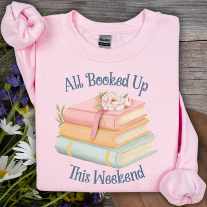 Light pink unisex sweatshirt with "All Booked Up This Weekend" text and watercolor stack of books.