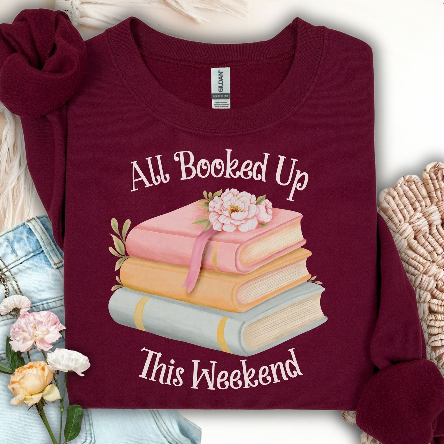 Maroon crewneck sweatshirt with "All Booked Up This Weekend" text and watercolor stack of books with flowers.