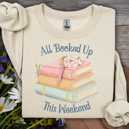 Sand crewneck sweatshirt with "All Booked Up This Weekend" text and watercolor stack of books.
