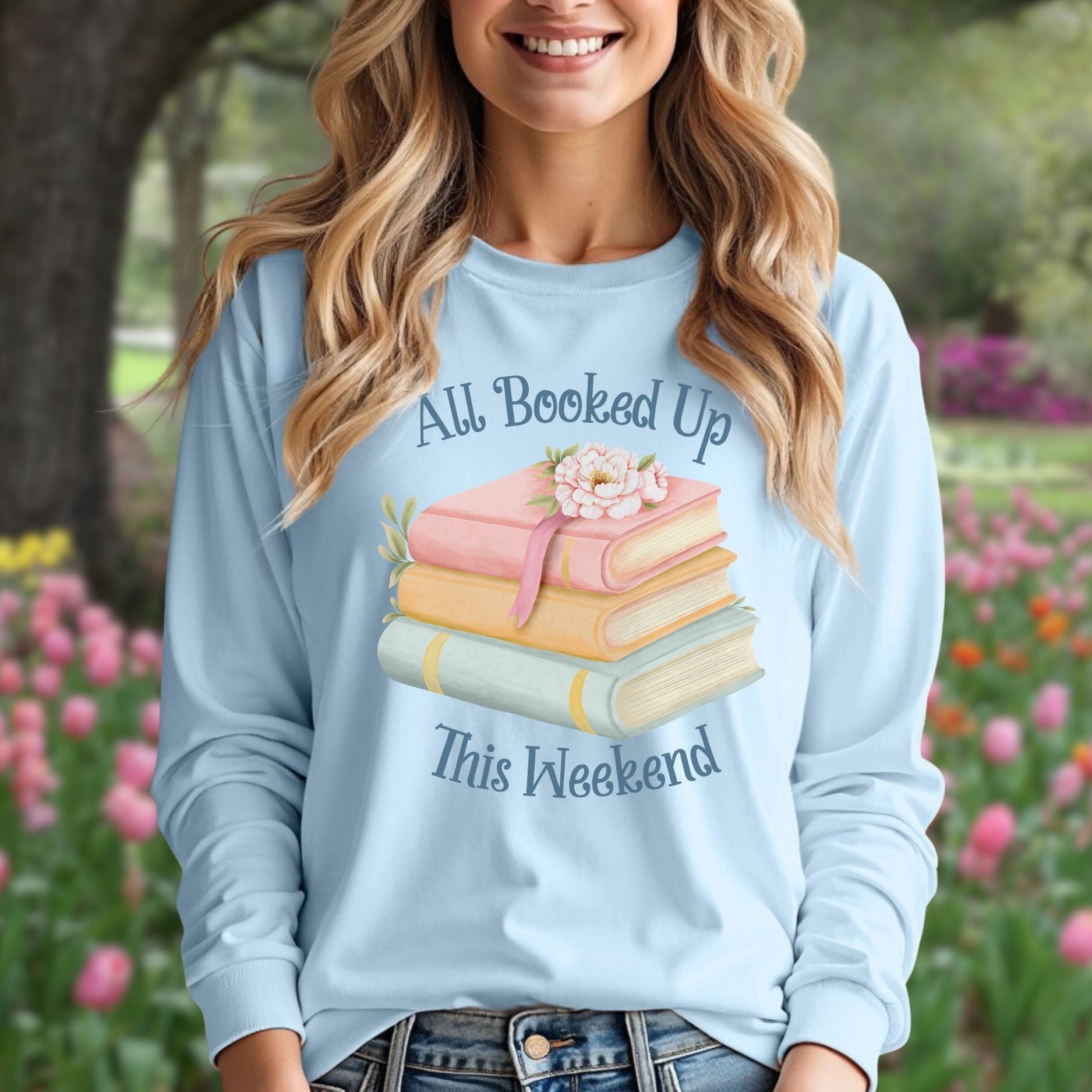 Light blue long sleeve tee with "All Booked Up This Weekend" text, pastel books, and a flower design.