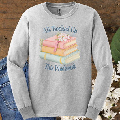 Ash gray long sleeve tee with "All Booked Up This Weekend" text and pastel book stack with a cat and flowers.