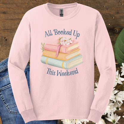 Light pink long sleeve tee with "All Booked Up This Weekend" text, pastel books, and a sleepy cat design.