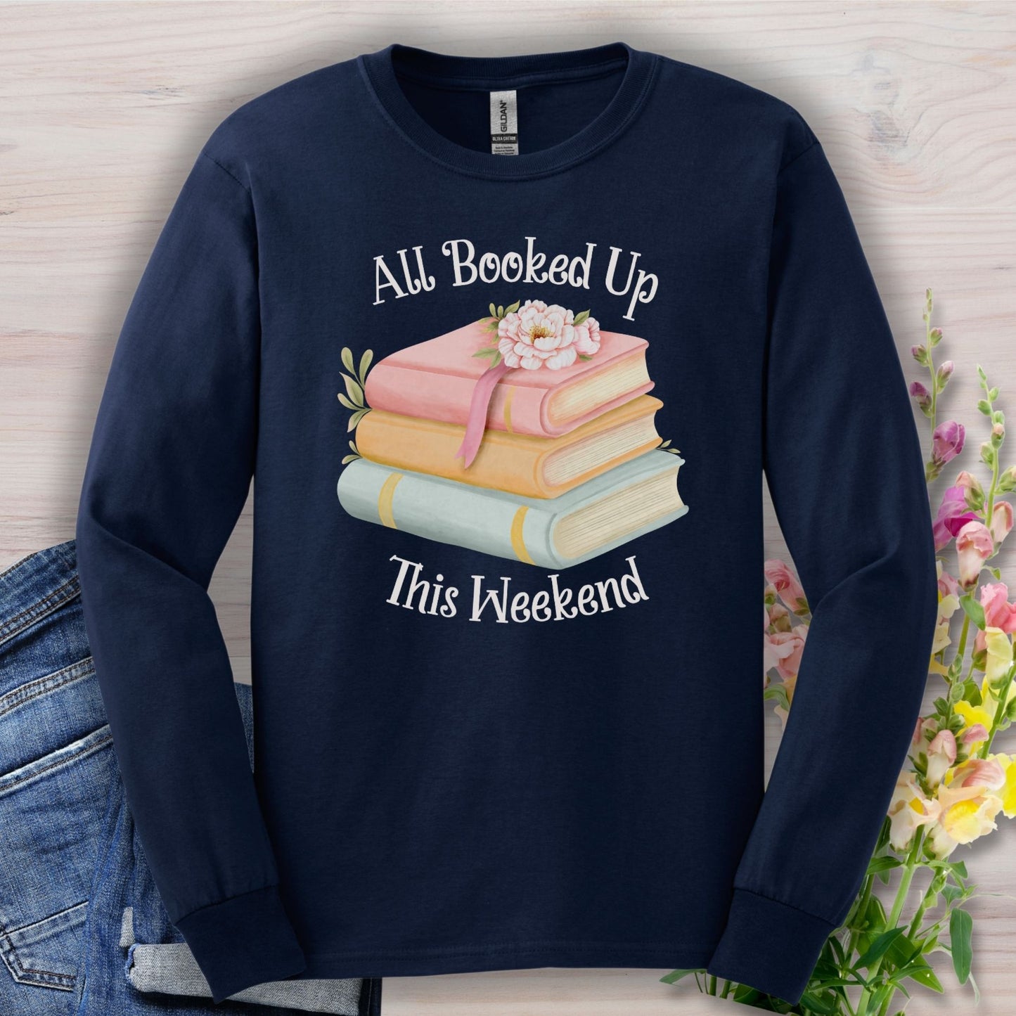 Navy long-sleeve tee with "All Booked Up This Weekend" text and a stack of pastel books with flowers.