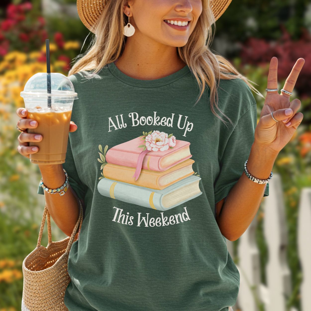 Woman in a relaxed-fit, garment-dyed dark green t-shirt with "All Booked Up This Weekend" and pastel books.