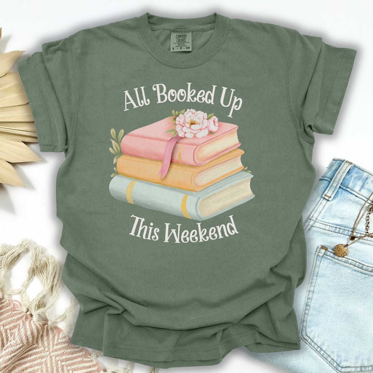 Moss green garment-dyed cotton t-shirt with "All Booked Up This Weekend" and pastel book stack design.