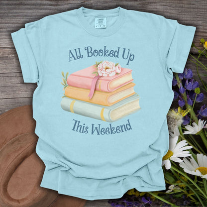 Chambray garment-dyed t-shirt with "All Booked Up This Weekend" text and a stack of pastel books with flowers.