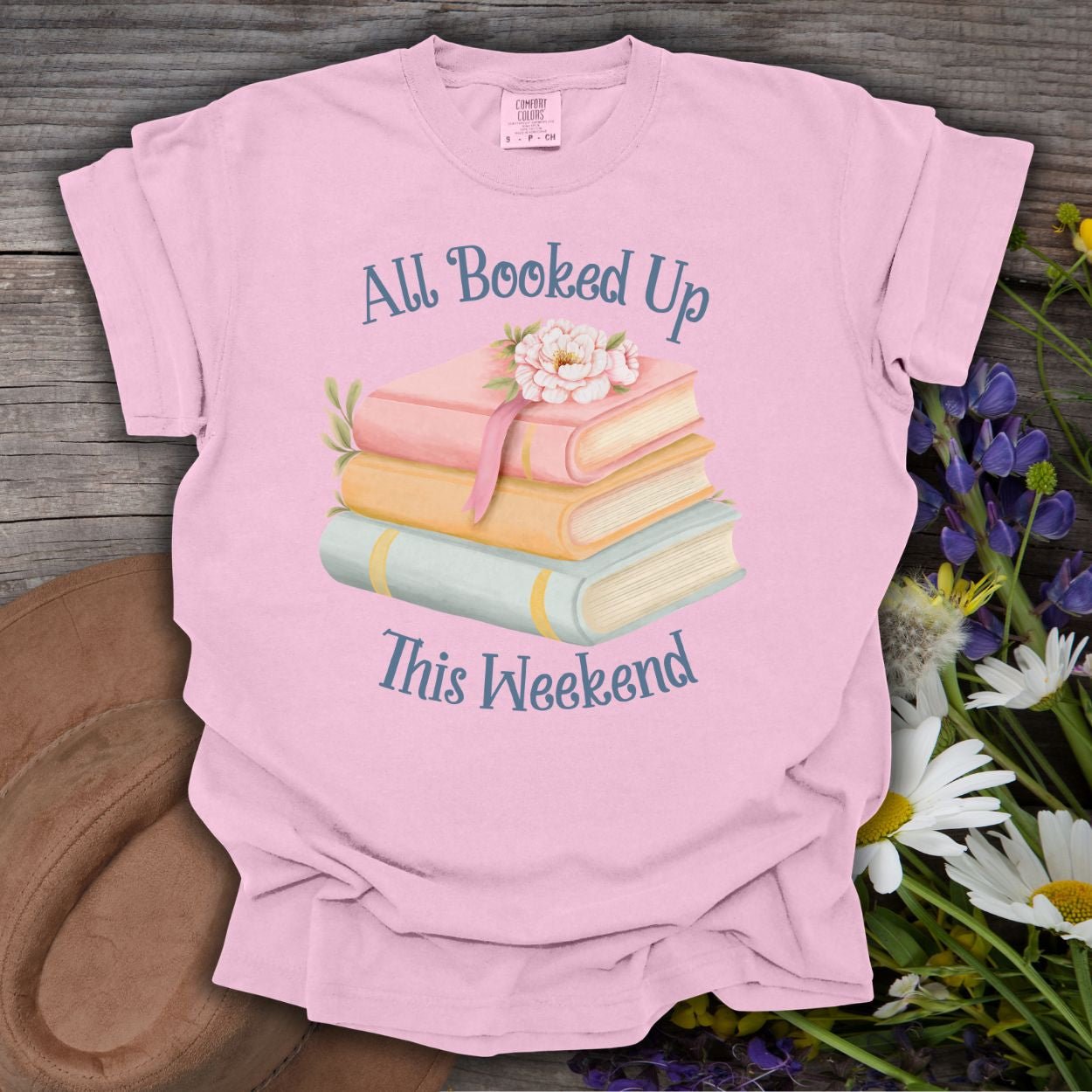 Blossom pink garment-dyed t-shirt with "All Booked Up This Weekend" text and pastel book stack design.