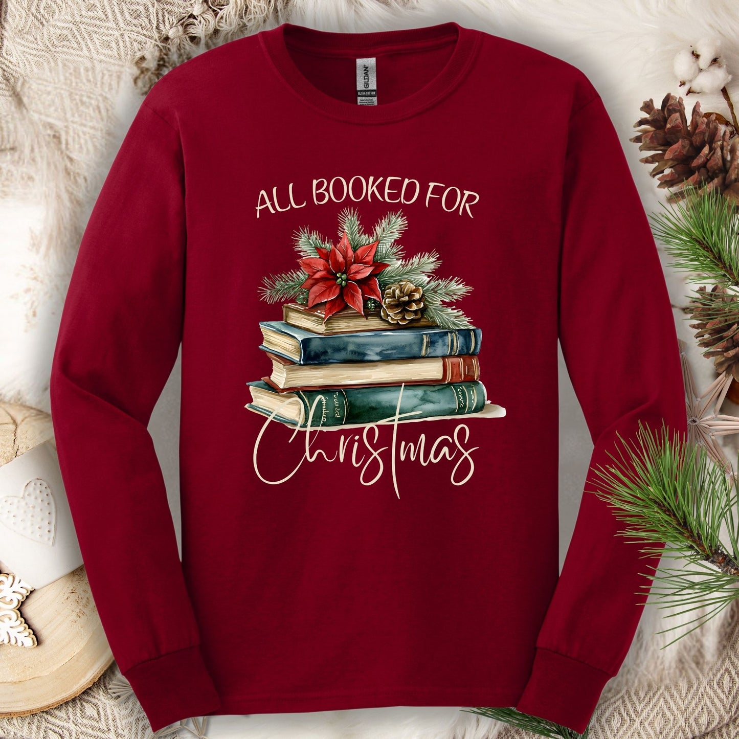 Cardinal Red long sleeve tee with "All Booked for Christmas" text and a watercolor stack of books with poinsettia.