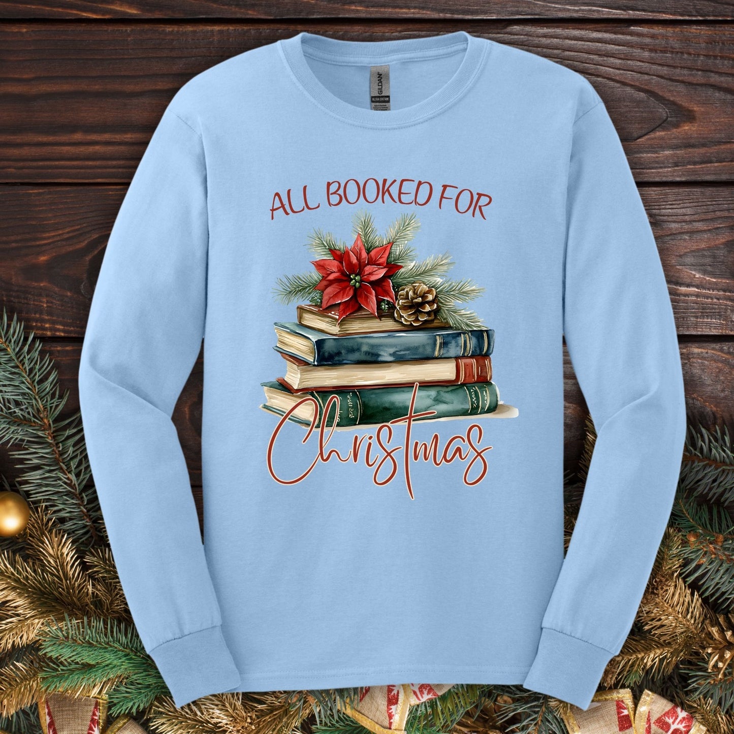 Light blue long sleeve tee with "All Booked for Christmas" text and a watercolor stack of books with poinsettia.