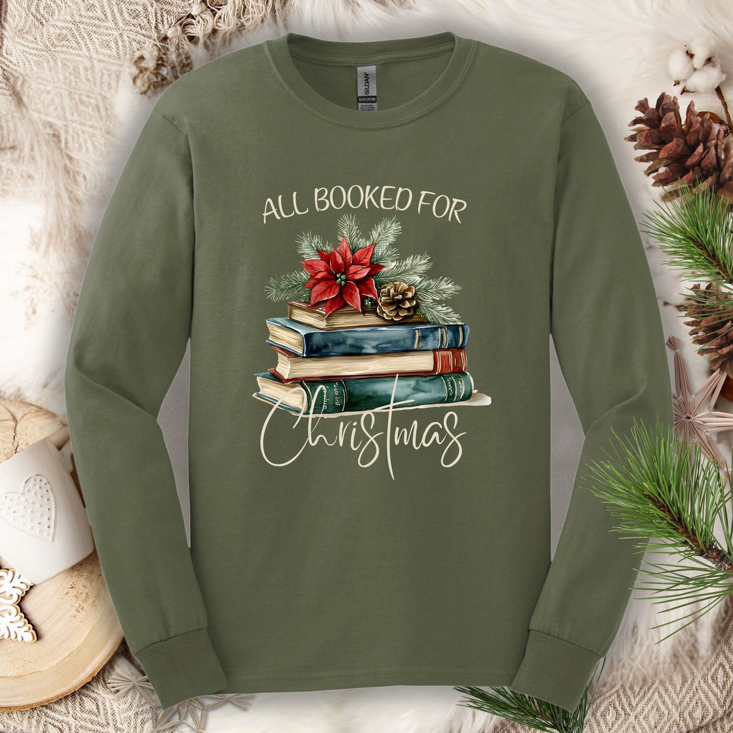 Military green long sleeve tee with a vintage watercolor stack of books, poinsettia, and "All Booked for Christmas" text.