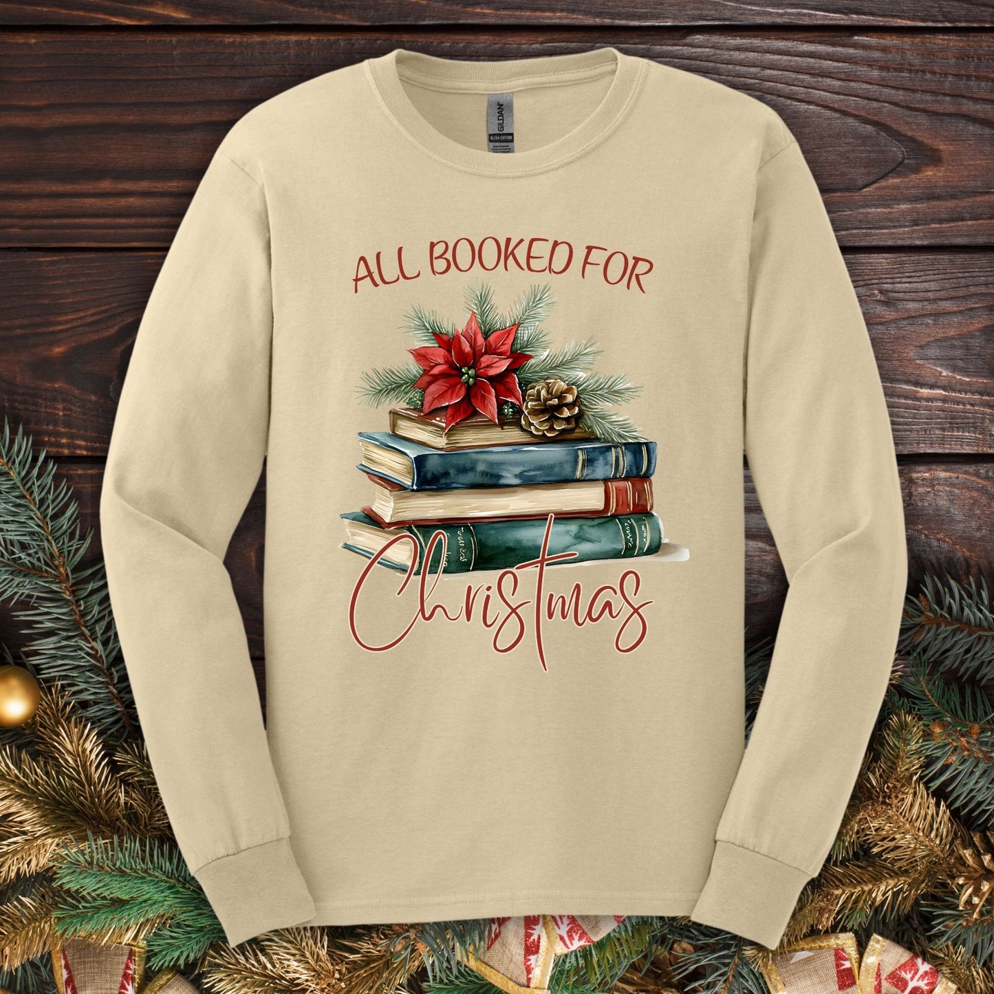 Sand long sleeve tee with "All Booked for Christmas" text and a watercolor stack of books with poinsettia.