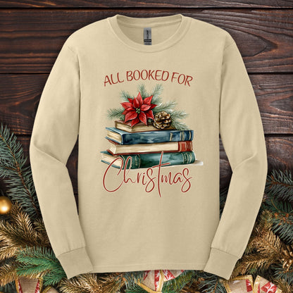 Sand long sleeve tee with "All Booked for Christmas" text and a watercolor stack of books with poinsettia.