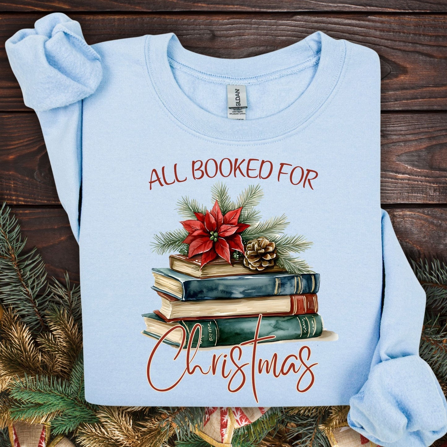Light blue fleece sweatshirt with "All Booked for Christmas" text and vintage watercolor holiday book stack design.