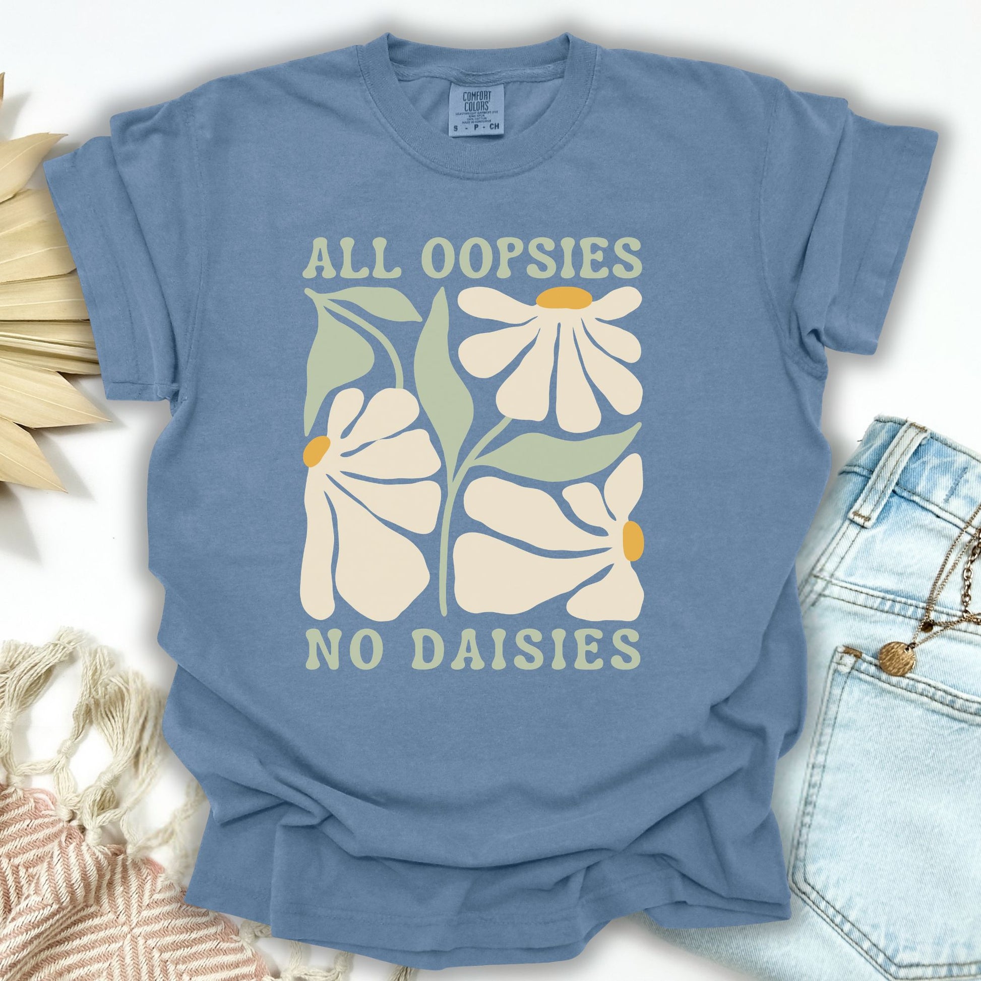 Blue Jean garment-dyed cotton t-shirt with "ALL OOPSIES NO DAISIES" text and retro floral design.