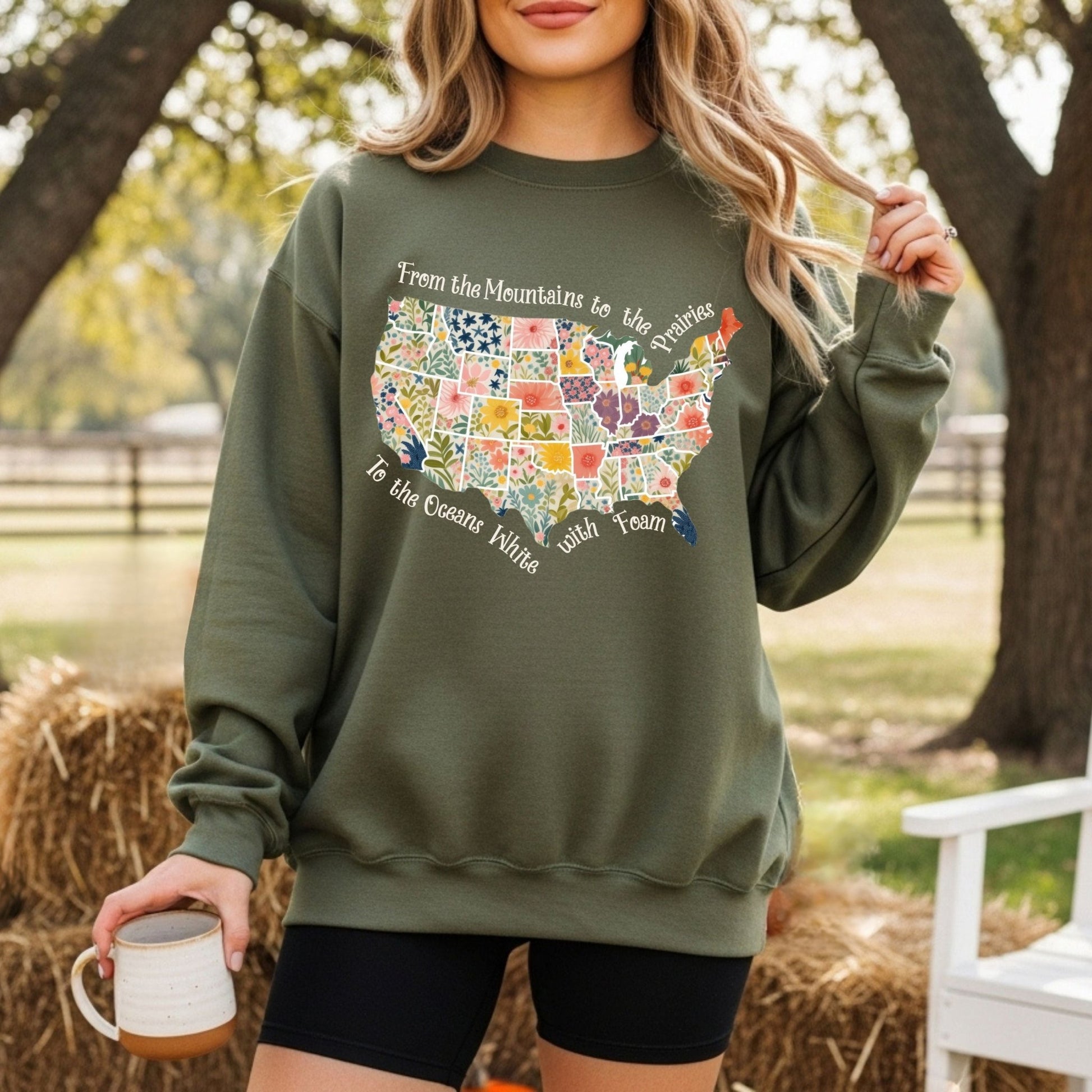 Olive green crewneck sweatshirt with a watercolor floral US map and "From the Mountains to the Prairies" text.