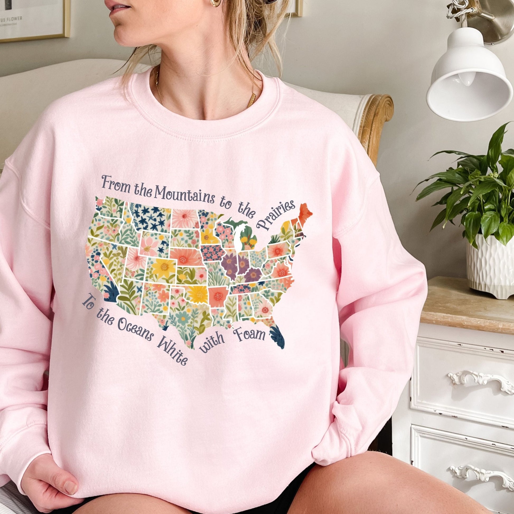 Pink crewneck sweatshirt with a watercolor floral map of the USA and "From the Mountains to the Prairies" text.