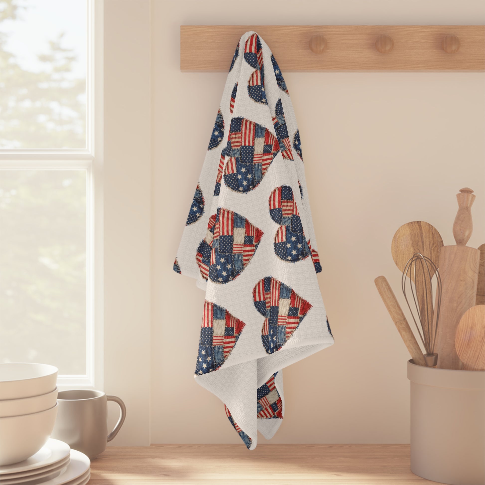 White microfiber tea towel with a repeating American flag patchwork heart pattern, hanging on a wooden peg.