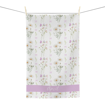 White microfiber tea towel with watercolor daisies, sweet peas, and "April" on a lavender band.