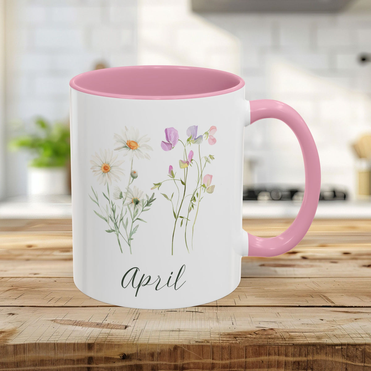 White ceramic mug with pink handle and interior, featuring watercolor daisies, sweet peas, and "April" text.