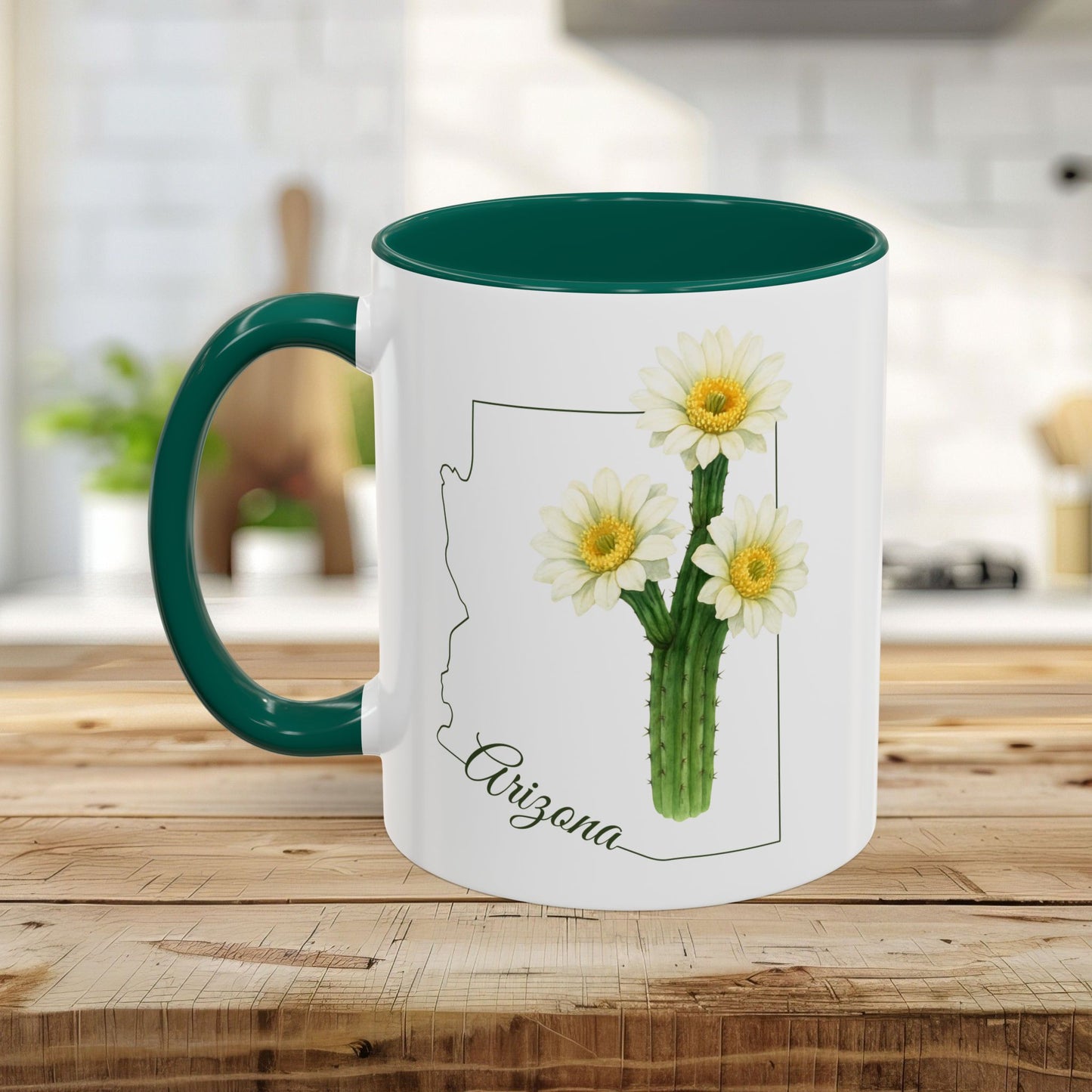 White ceramic mug with a green handle and interior, featuring an Arizona outline and blooming saguaro cactus.